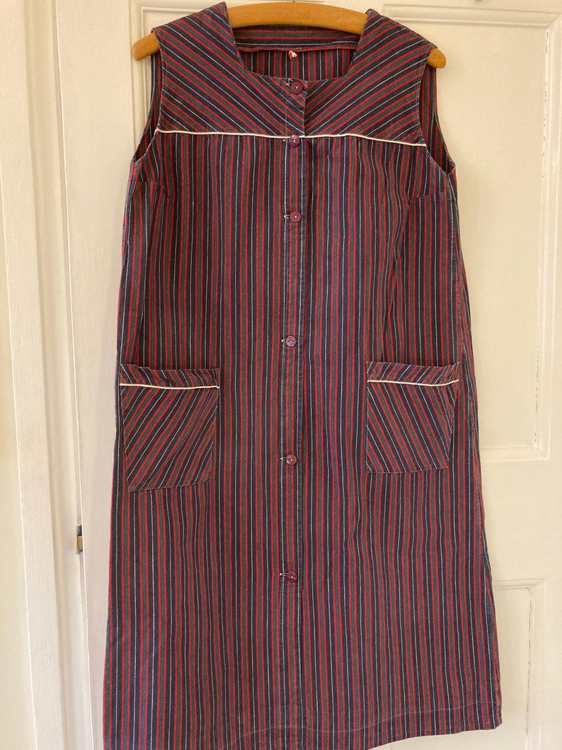 May include: A long, sleeveless dress with a button-up front and two pockets. The dress is made of a striped fabric in shades of red, black, and white.