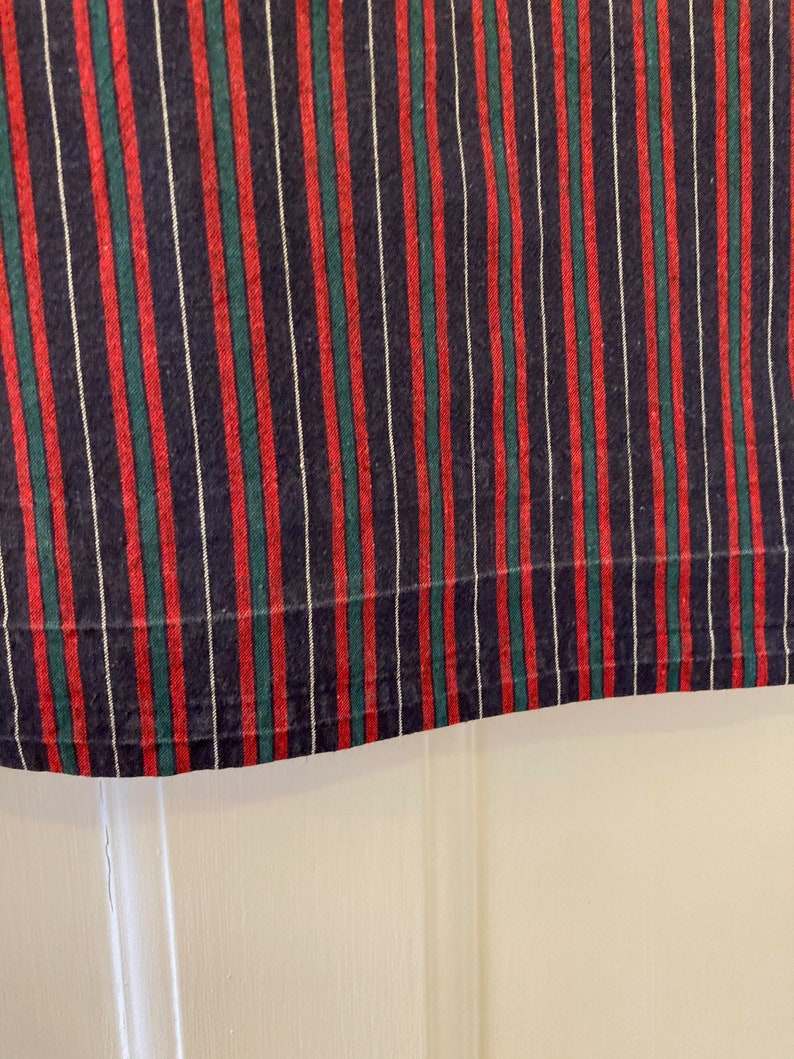 May include: Close-up of a striped fabric with red, green, and white stripes on a dark blue background.