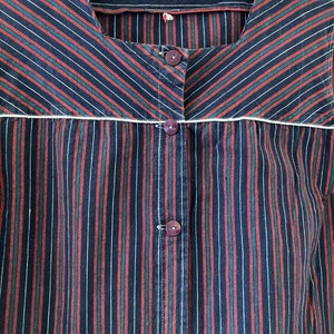 May include: A striped shirt with a white trim around the neckline. The shirt has red, green, and black stripes. The shirt has a button closure.
