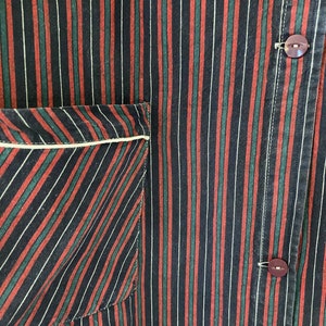 May include: A close-up of a black, red, and green striped fabric with a white pocket. The fabric has a subtle diagonal pattern. Two dark brown buttons are visible on the right side of the image.
