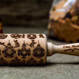 May include: A wooden rolling pin with a Christmas-themed design featuring ornaments, cats, and stars. The handle is engraved with the text "Oma Marta".