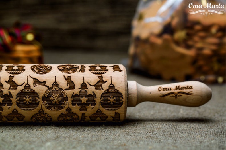 May include: A wooden rolling pin with a Christmas-themed design featuring ornaments, cats, and stars. The handle is engraved with the text "Oma Marta".