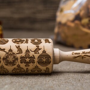 May include: A wooden rolling pin with a Christmas-themed design featuring cats, ornaments, and snowflakes. The handle is engraved with the text "Oma Marta".
