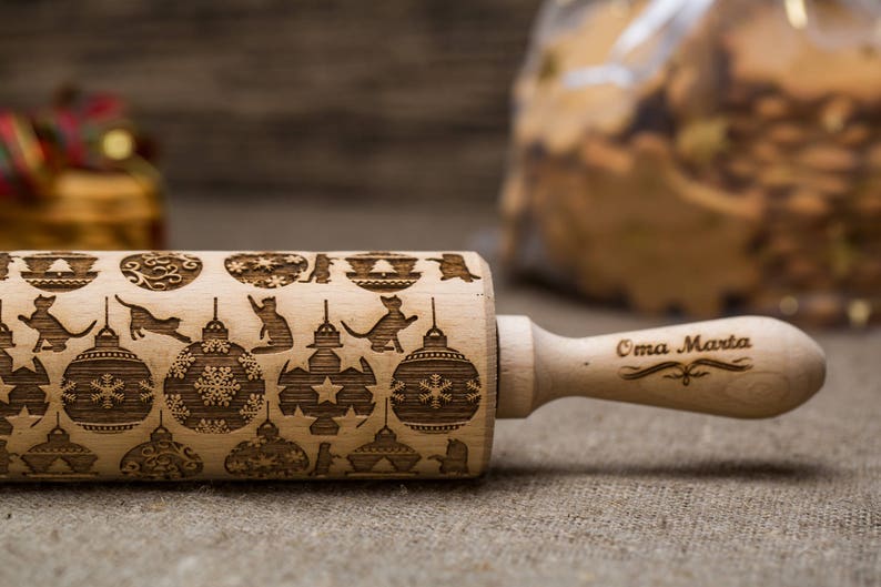May include: A wooden rolling pin with a Christmas-themed design featuring cats, ornaments, and snowflakes. The handle is engraved with the text "Oma Marta".