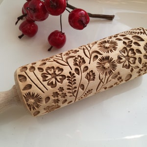 Puede incluir: Un rodillo de madera con un diseño floral tallado en la superficie. El rodillo está sobre una superficie blanca.