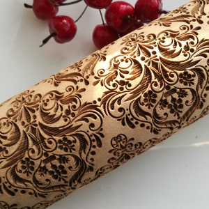 May include: A wooden rolling pin with a detailed, intricate, carved design of a floral pattern. The design is in shades of brown and black.