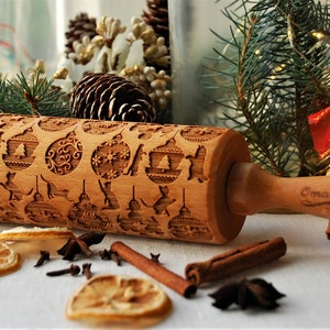May include: A wooden rolling pin with a Christmas-themed design. The rolling pin is engraved with images of ornaments, reindeer, and snowflakes. The handle is engraved with the words "Emma Made".