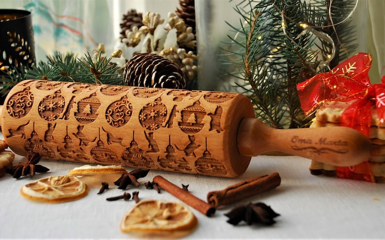 May include: A wooden rolling pin with a Christmas-themed design. The rolling pin is engraved with images of ornaments, reindeer, and snowflakes. The handle is engraved with the words "Emma Made".