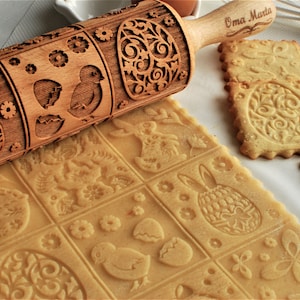 Può includere: Un mattarello di legno con un design pasquale inciso, tra cui coniglietti, uova e pulcini. Il mattarello viene utilizzato per creare motivi decorativi sulla pasta frolla. Il testo "Oma Marta" è inciso sul manico.