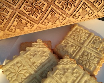Pode incluir: Close-up de quatro biscoitos com um padrão de floco de neve, feitos com um rolo de madeira com um design de floco de neve. Os biscoitos são de cor castanho claro e o rolo é de cor madeira natural.