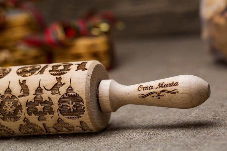 May include: A wooden rolling pin with a Christmas-themed design, including ornaments and cats. The handle is engraved with the text "Oma Marta".