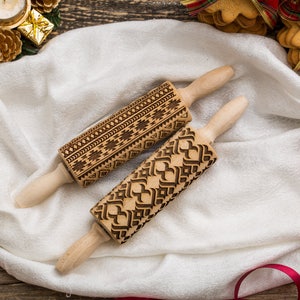 May include: Two wooden rolling pins with intricate engraved designs. One pin features a geometric pattern, while the other has a repeating heart design. Both pins are on a white cloth with red ribbon.