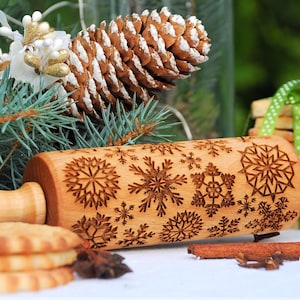 May include: A wooden rolling pin with a snowflake design and the text "Oma Marta" engraved on the handle. The rolling pin is surrounded by cookies, cinnamon sticks, and star anise.