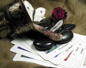 May include: A black and gold metal bowl, a white butterfly figurine, a dark red rose, a clear quartz crystal, and smooth black stones resting on a fan of tarot cards labeled The Priestess, The Magus, Death, and Change, with a wooden wand.
