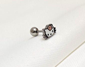 Puede incluir: Un pendiente de barra de metal plateado con un dije plano en forma de personaje. El dije es blanco con contornos negros, ojos negros y un pequeño detalle de flor rosa en el lateral. El pendiente incluye un cierre de bola de metal liso y redondo.