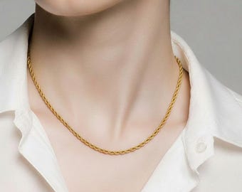 Puede incluir: Un collar de cadena de cuerda de color dorado. El collar lo lleva una persona que lleva una camisa blanca con cuello. La cadena tiene un diseño retorcido y se asienta cerca del cuello.
