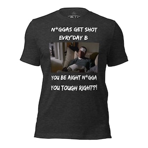 May include: A dark heather grey t-shirt with a white graphic print of a man with a bandage on his forehead. The text on the shirt reads "N*GGAS GET SHOT EVRY'DAY B YOU BE AIGHT N*GGA YOU TOUGH RIGHT?!"