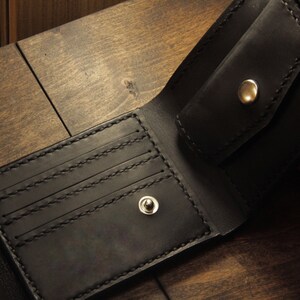 May include: A black leather wallet with multiple card slots and a flap closure. The wallet has two silver metal snaps.