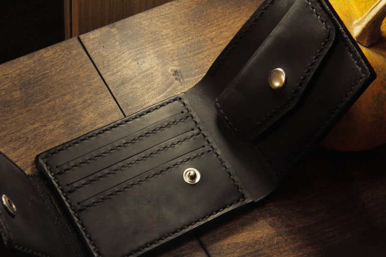 May include: A black leather wallet with multiple card slots and a flap closure. The wallet has two silver metal snaps.
