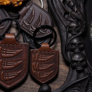 May include: Close-up of five brown leather keychains featuring a design of three claws. The keychains are displayed on a wooden surface with a black background.