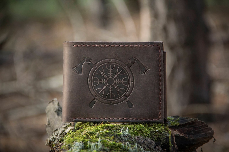 May include: A brown leather wallet with a stitched border and a design of a shield with a symbol and two axes.