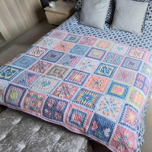 Könnte beinhalten: Eine handgefertigte Häkeldecke mit einem Patchwork-Design. Die Decke besteht aus Quadraten in Pastellfarben, darunter Rosa, Blau, Gelb und Weiß. Die Quadrate sind in einem Rastermuster angeordnet und erzeugen eine gemütliche und einladende Optik. Die Decke liegt auf einem Bett.