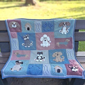 Peut inclure: Une couverture en crochet aux couleurs bleu, rose et blanc présente différentes races de chiens, dont un caniche, un teckel et un schnauzer. La couverture est faite de fil doux et a une surface texturée.