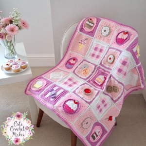 May include: A handmade crochet blanket in shades of pink, white, and purple, featuring squares with various dessert designs like cupcakes and donuts. The blanket is draped over a white chair, with a floral arrangement and cupcakes in the background. The text "Cute Crochet Makes" is visible.