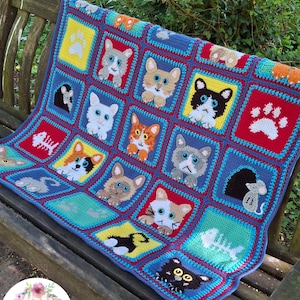 May include: A multi-colored crochet blanket featuring a grid of square panels with various cat faces, paw prints, fish skeletons, and mice. The squares are bordered in blue and red, showcasing diverse feline expressions and animal-themed motifs.
