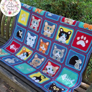 May include: A multi-colored crochet blanket featuring a grid of square panels. Each square displays a different cat face, a white paw print, a fish skeleton, or a mouse in a hole. The blanket uses vibrant red, yellow, blue, and teal yarn colors.