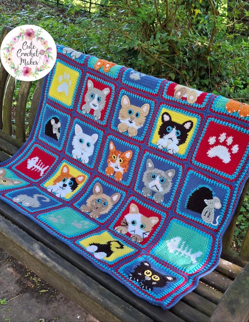 May include: A multi-colored crochet blanket featuring a grid of square panels. Each square displays a different cat face, a white paw print, a fish skeleton, or a mouse in a hole. The blanket uses vibrant red, yellow, blue, and teal yarn colors.