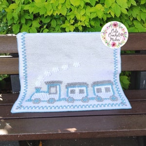 May include: A white crochet baby blanket with a blue border and a train design featuring gray and white cars. The blanket has white puff balls for clouds and the text "Cute Crochet Makes" is on a circle with pink flowers.