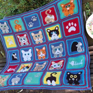 May include: A handmade crochet blanket featuring a grid of colorful squares, each displaying various cat-themed designs including cat faces, paw prints, fish skeletons, and mice. The blanket has a blue border and includes a circular logo reading Cute Crochet Makes.