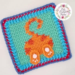 May include: A square crochet granny square featuring a central orange cat rear end motif with a raised tail and two paws on a light teal background. The border consists of alternating rows of bright blue, magenta, and dark blue yarn stitches.