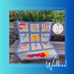 May include: A crocheted blanket featuring a pattern of dachshund dogs in various poses and colors. The blanket is gray with blue and red accents. The text "Walkies!" is written at the bottom of the blanket. The blanket is on a wooden bench with green plants in the background.