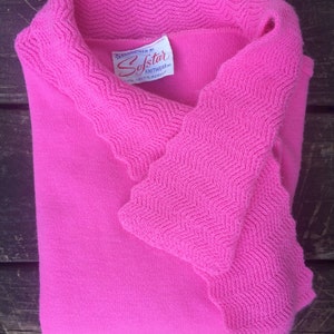 May include: A pink knitted sweater with a scalloped collar and a label that reads "Fashioned by Softstar Knitwear 100% Orlon Acrylic".