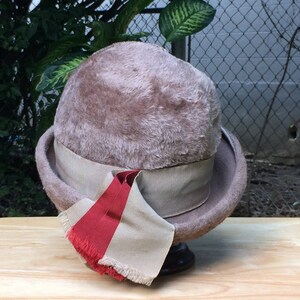 May include: A brown felt hat with a wide brim and a beige ribbon. The hat has a red and beige ribbon tied around it.