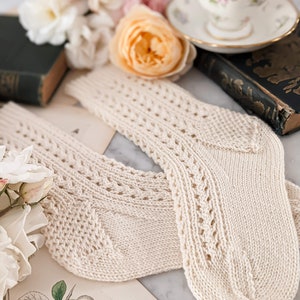 Peut inclure: Une paire de chaussettes en tricot cr&egrave;me avec des d&eacute;tails ajour&eacute;s. Les chaussettes sont pr&eacute;sent&eacute;es sur une surface en marbre avec des illustrations botaniques vintage, des roses et une tasse &agrave; th&eacute;. Les chaussettes ont un aspect textur&eacute; et un design classique.