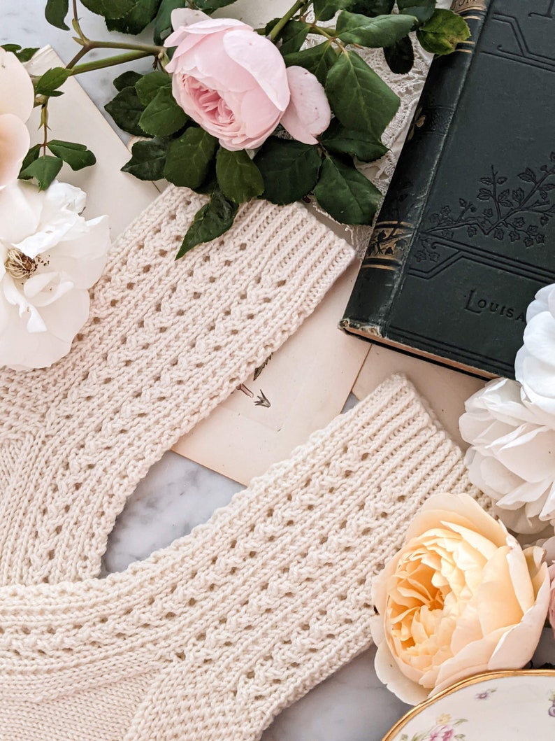 Peut inclure: Chaussettes en tricot cr&egrave;me avec un motif ajour&eacute; d&eacute;coratif. Les chaussettes sont pr&eacute;sent&eacute;es avec des roses roses et blanches, des livres anciens et de la papeterie ancienne, cr&eacute;ant une esth&eacute;tique romantique et vintage.