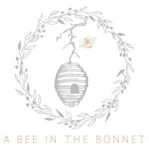 Peut inclure: Logo avec une abeille, une ruche et une couronne florale dans des tons de gris et d'or sur fond blanc. Le texte "A BEE IN THE BONNET" est en bas, en or clair.
