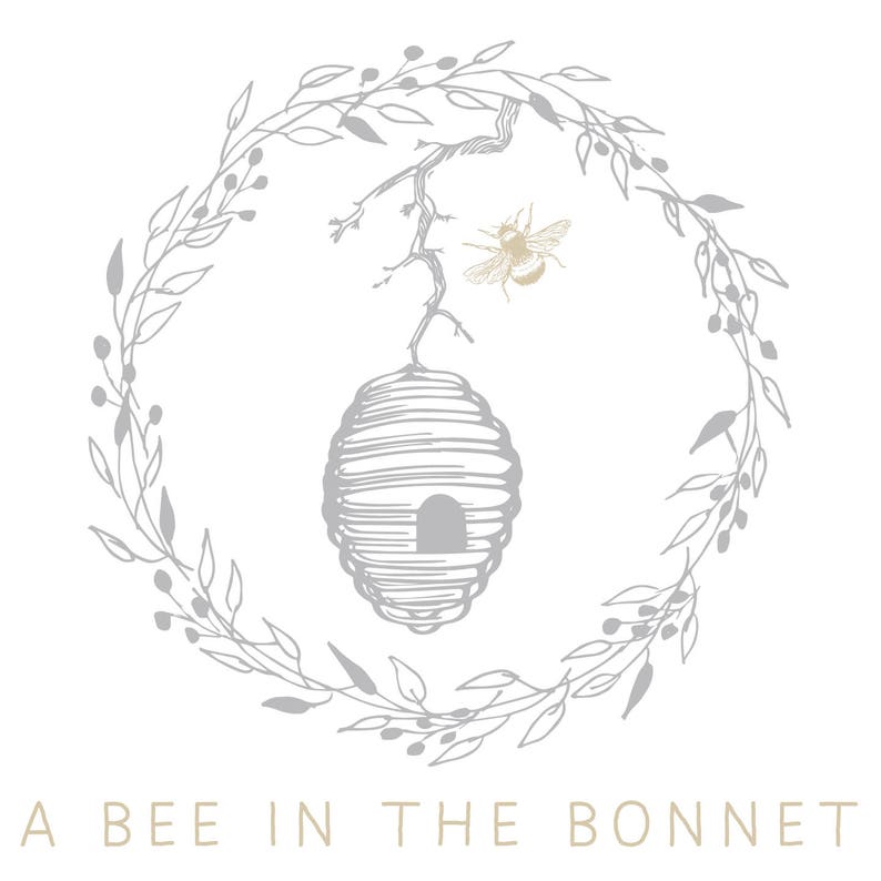 Peut inclure: Logo avec une abeille, une ruche et une couronne florale dans des tons de gris et d'or sur fond blanc. Le texte "A BEE IN THE BONNET" est en bas, en or clair.