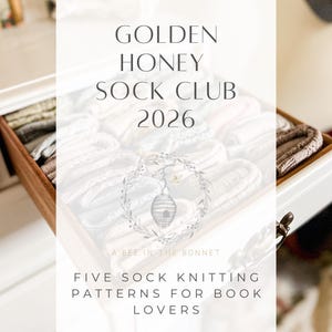 May include: A white box with a wooden interior is filled with folded socks in various neutral colors. The text "GOLDEN HONEY SOCK CLUB 2026" is displayed on the front of the box, along with "FIVE SOCK KNITTING PATTERNS FOR BOOK LOVERS."