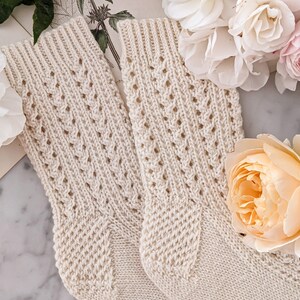 Peut inclure: Une paire de chaussettes en tricot cr&egrave;me avec un motif ajour&eacute; d&eacute;licat. Les chaussettes sont entour&eacute;es de roses roses et blanches, cr&eacute;ant une esth&eacute;tique chaleureuse et f&eacute;minine. Les chaussettes ont des poignets c&ocirc;tel&eacute;s et un design textur&eacute;.