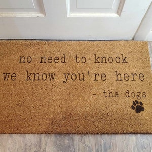 May include: A brown coir doormat with the text "no need to knock we know you're here - the dogs" and a black paw print.
