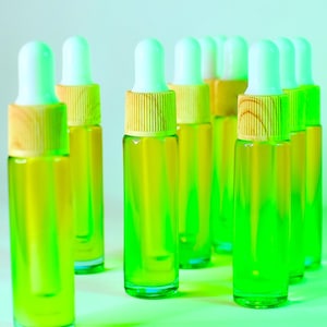 May include: A collection of small glass dropper bottles filled with a vibrant green liquid. Each bottle has a white dropper top and a wooden collar. The bottles are arranged on a light green surface.