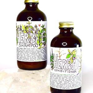 May include: Two brown glass bottles with gold lids, labeled "Herbal Shampoo" and "Herbal Conditioner". Both bottles feature hand-drawn illustrations of plants and flowers. The bottles are sitting on a white surface.