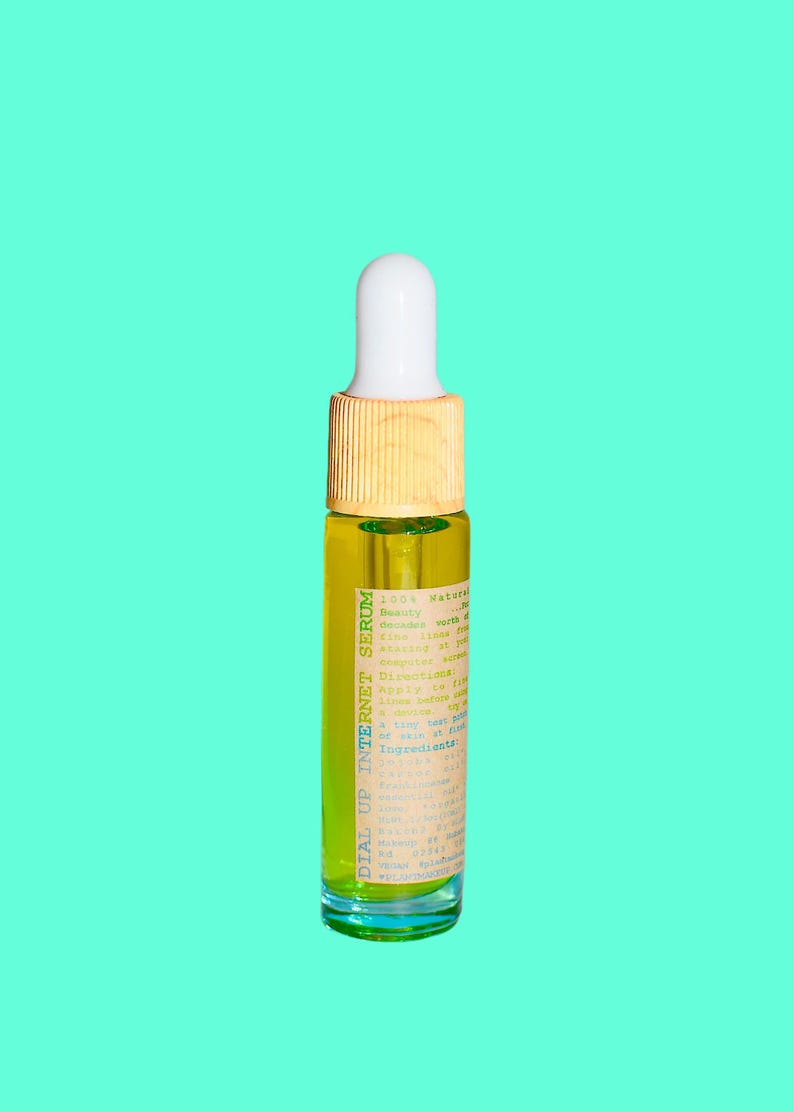 May include: A small glass bottle of serum with a white dropper top and a wooden collar. The bottle contains a yellow liquid and has a label with the text "DIAL UP INTERNET SERUM". The background is a solid teal color.