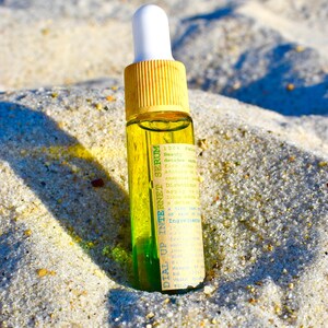May include: A small glass bottle of serum with a yellow cap and white dropper. The bottle is filled with a clear liquid and a green liquid at the bottom. The label reads "DIAL UP INTERNET SERUM". The bottle is resting on sand.
