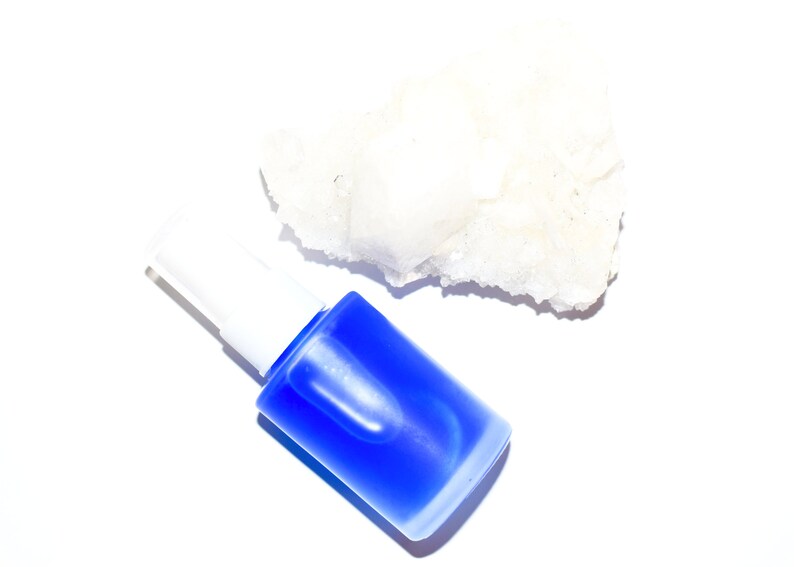 May include: A blue glass bottle with a white pump top and a white, rough-textured rock.