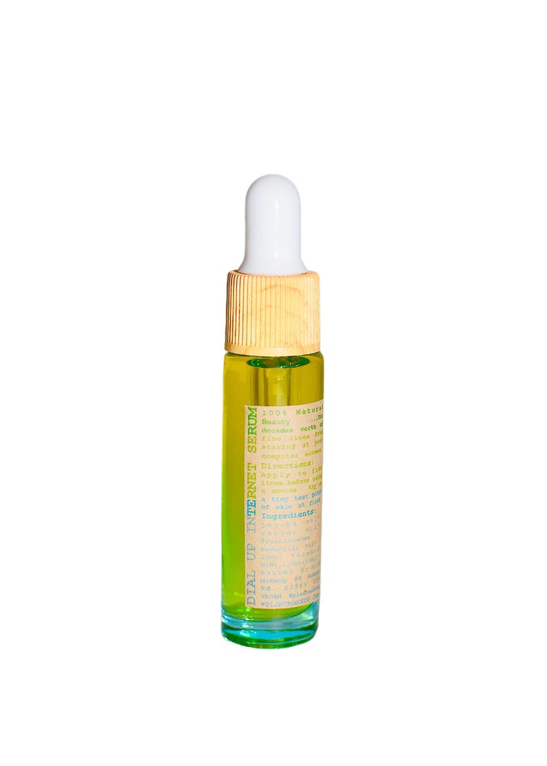May include: A small, clear glass bottle filled with a yellow liquid, labeled "DIAL UP INTERNET SERUM." The bottle has a white dropper top and a light brown wooden cap. The label includes text about the product's ingredients and directions.